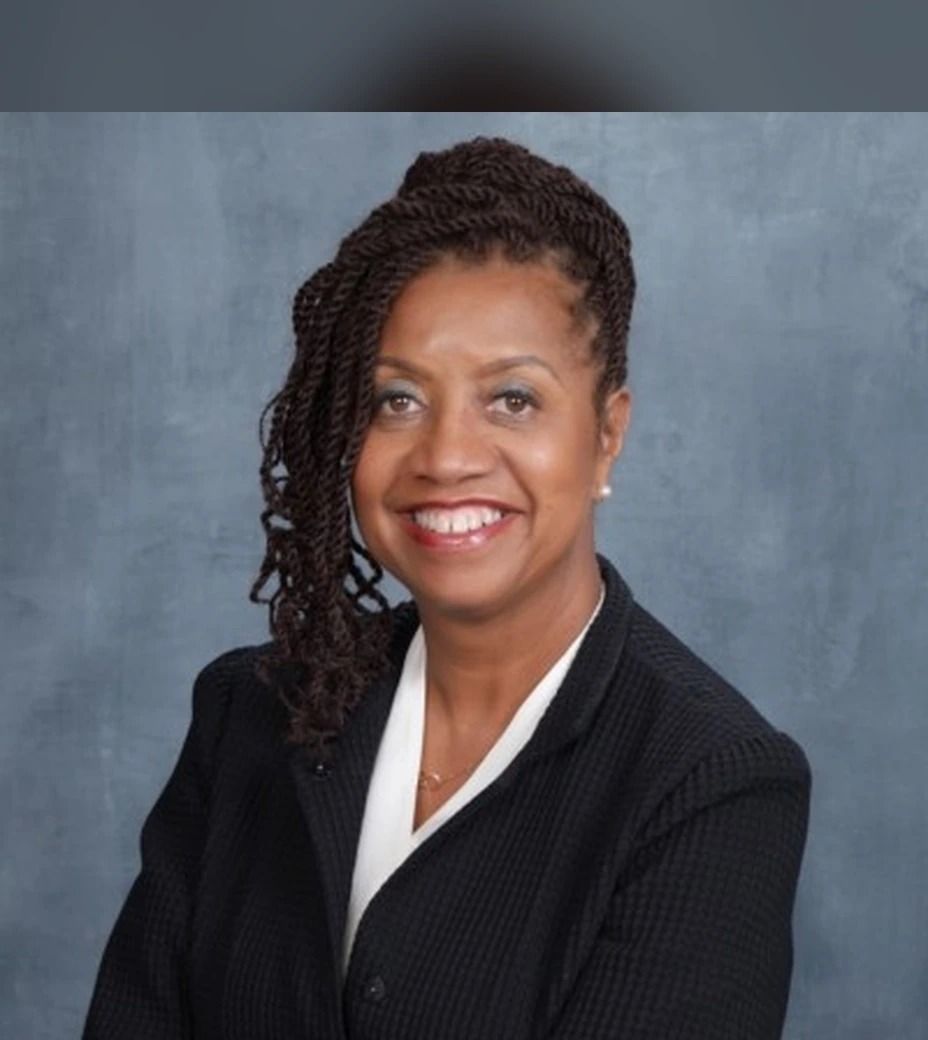 Dr. Carol J. Scott in a dark blazer, smiling, against a gray studio backdrop.